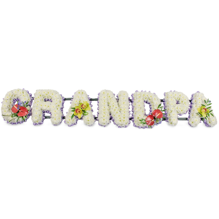 The image shows a bespoke funeral flower arrangement spelling out "GRANDPA" in proud, capital letters, laid out in a straight horizontal line as if ready to rest by a coffin during a service in Hither Green. Every letter is built from a dense carpet of small, white chrysanthemum heads, each bloom carefully placed so the petals overlap and interlock, creating a smooth, full texture that feels both soft and substantial. The brightness of the white flowers contrasts gently with a trim of light lavender ribbon that runs along the base of each letter, the lilac edging providing a delicate frame and a hint of colour without overpowering the calm, dignified mood. Hidden behind the flowers, slim dark green bars and frames connect and support the letters, giving the tribute enough strength to be carried from a florist's studio in Hither Green to a local church, crematorium, or cemetery with ease. Colourful accent sprays are thoughtfully positioned to punctuate the white. On the G at the far left, a bold cluster of deep red anthuriums with glossy, heart-shaped spathes and golden-yellow spadices sits among rich green leaves, suggesting love and gratitude. The first A carries a softer spray of yellow-green orchids, their elegant petals and pale throats arranged with lush foliage to add movement and refinement. The central D repeats the dramatic red anthuriums, balancing the design, while the final A on the right mirrors the orchid cluster, bringing the piece full circle. This personalised "GRANDPA" tribute, crafted with the precision of an experienced local florist in Hither Green, is designed to offer family and friends a touching, visually striking way to honour a beloved grandfather's life and memory during a funeral, wake, or graveside committal.
